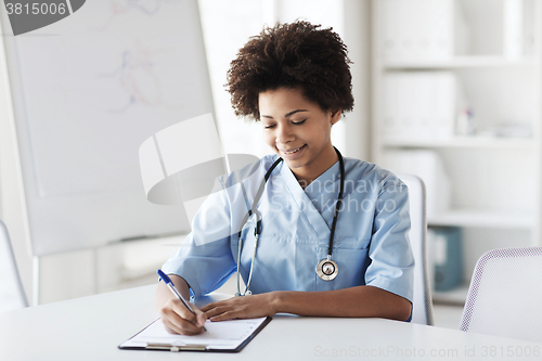 Image of happy female doctor or nurse writing to clipboard