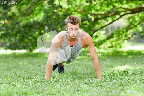 Image of young man doing push ups on grass in summer park