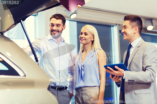 Image of happy couple with car dealer in auto show or salon