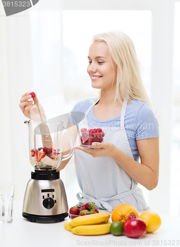 Image of smiling woman with blender preparing shake at home