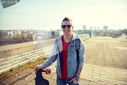 Image of smiling man or teenager with longboard on street
