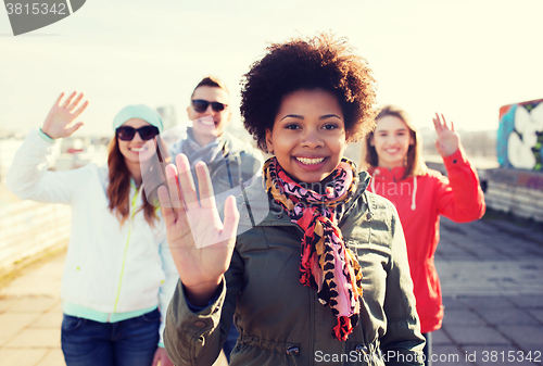 Image of happy teenage friends waving hands on city street