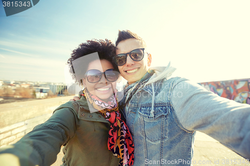 Image of happy teenage couple taking selfie on city street