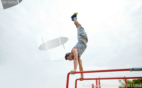 Image of young man exercising on parallel bars outdoors