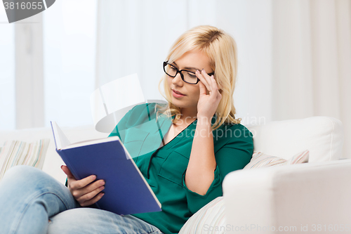 Image of young woman in glasses reading book at home