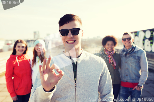 Image of happy teenage friends showing ok sign on street