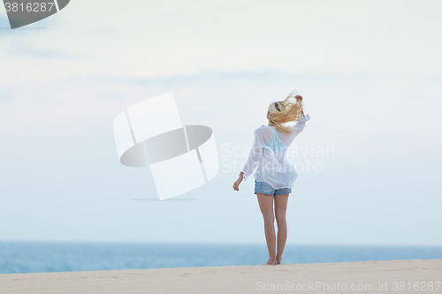 Image of Woman on sandy beach in white shirt in morning. 