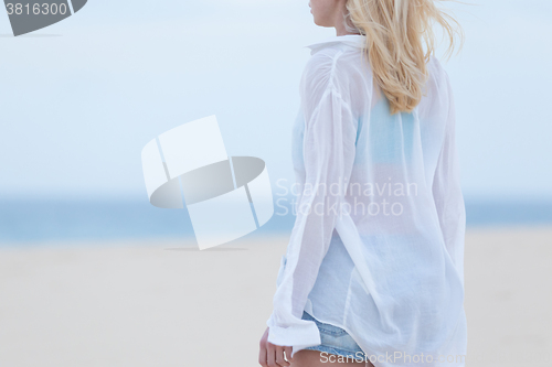 Image of Woman on sandy beach in white shirt at dusk. 