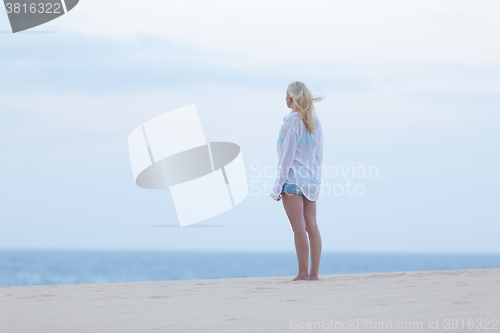 Image of Woman on sandy beach in white shirt at dusk. 