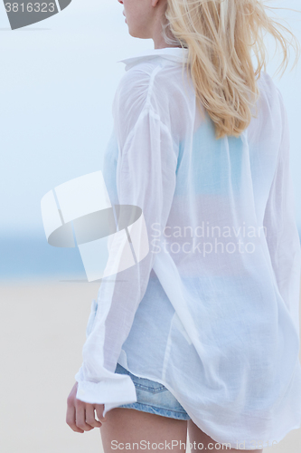 Image of Woman on sandy beach in white shirt at dusk. 