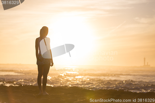 Image of Woman on sandy beach watching sunset.
