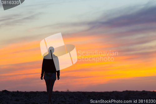 Image of Woman on rocky beach watching sunset.