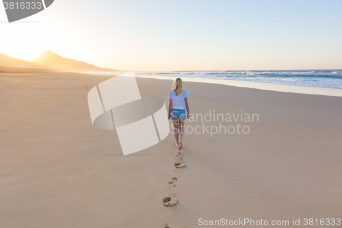 Image of Lady walking on sandy beach in sunset.