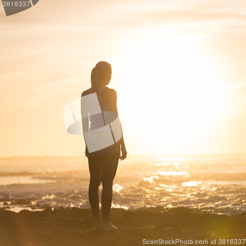 Image of Woman on sandy beach watching sunset.