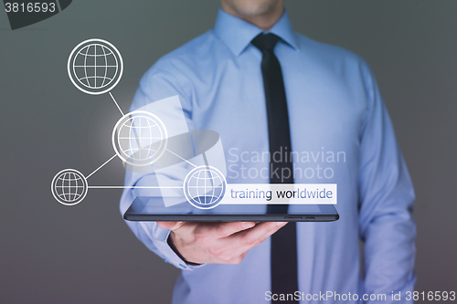 Image of Businessman holding a tablet pc with worldwide training text on virtual screen. Internet and Business concept.