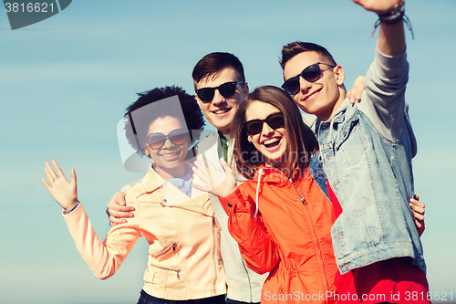 Image of happy teenage friends in shades waving hands