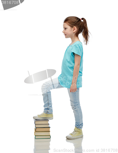 Image of happy little girl stepping on book pile