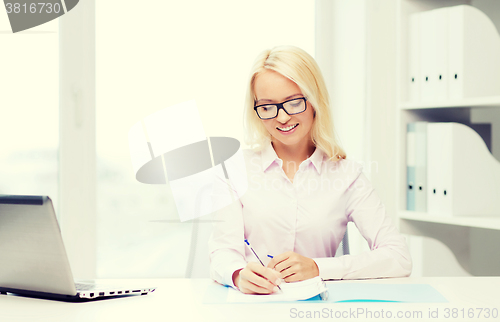 Image of smiling businesswoman reading papers in office