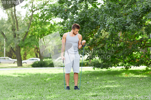 Image of young man exercising with expander in summer park