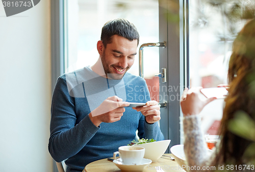 Image of happy couple picturing food by smartphone at cafe