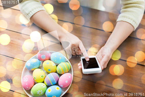 Image of close up of hands with easter eggs and smartphone