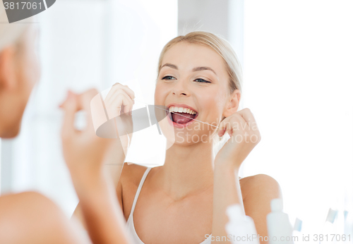 Image of woman with dental floss cleaning teeth at bathroom