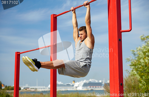 Image of young man exercising on horizontal bar outdoors