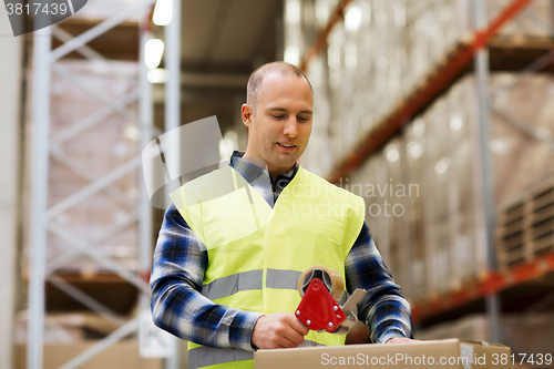 Image of man in safety vest packing box at warehouse