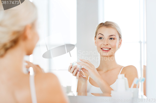 Image of happy woman applying cream to face at bathroom