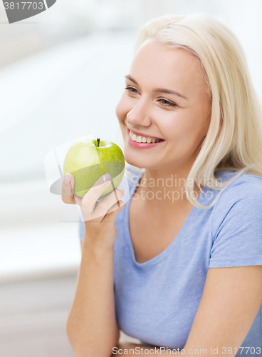 Image of happy woman eating green apple at home