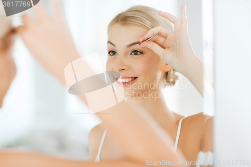 Image of woman with tweezers tweezing eyebrow at bathroom