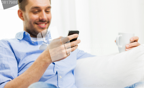 Image of smiling man texting message on smartphone at home