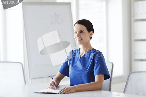 Image of happy female doctor or nurse writing to clipboard