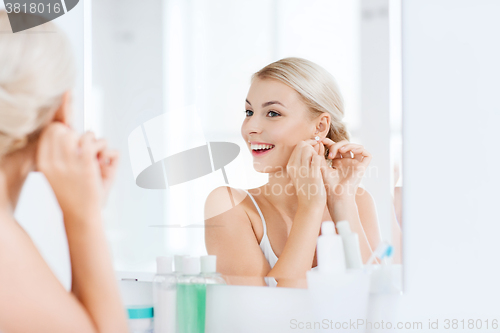 Image of woman trying on earring looking at bathroom mirror