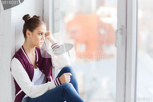 Image of sad pretty teenage girl sitting on windowsill