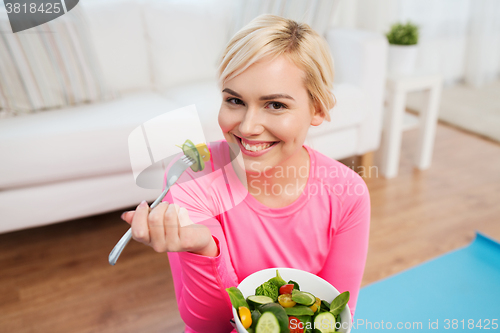 Image of smiling young woman eating salad at home