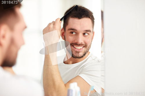 Image of happy man brushing hair  with comb at bathroom