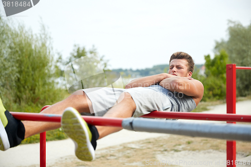 Image of young man doing sit up on parallel bars outdoors