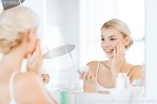 Image of happy woman applying cream to face at bathroom