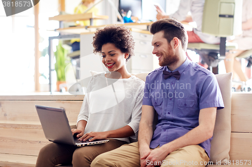 Image of happy creative team with laptop in office