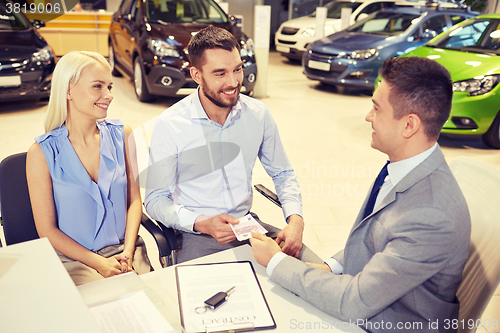 Image of happy couple with car dealer in auto show or salon