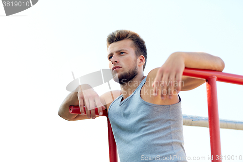 Image of young man exercising on parallel bars outdoors