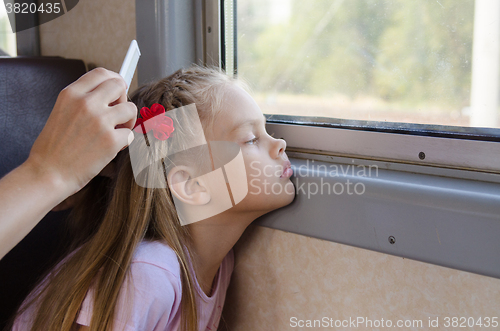 Image of A sad little girl looks at the window while sitting in an electric train until my mother combs her long hair