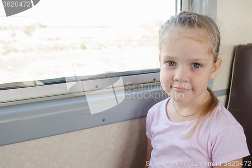 Image of Happy girl sitting on a chair by the window in a suburban electric train