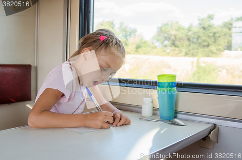 Image of Girl draws a pen on a sheet of paper in a second-class train carriage