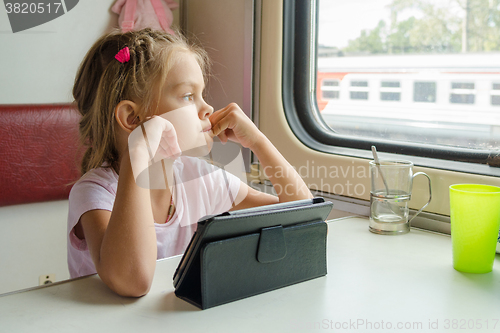 Image of Girl thoughtfully looked out the window while sitting with a tablet on a train