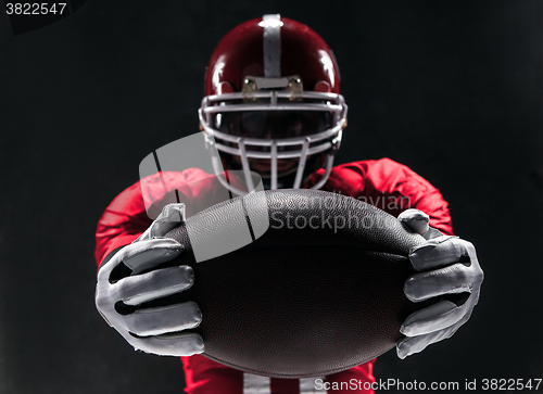 Image of American football player posing with ball on black background