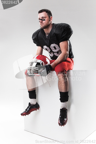 Image of American football player sitting with  helmet on white background