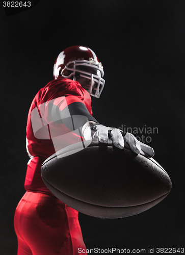 Image of American football player posing with ball on black background