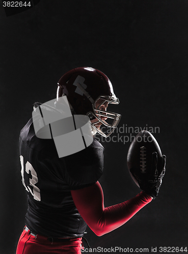 Image of American football player posing with ball on black background